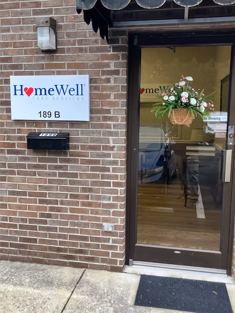 Brick exterior entrance of HomeWell Care Services with a hanging flower basket by the door.