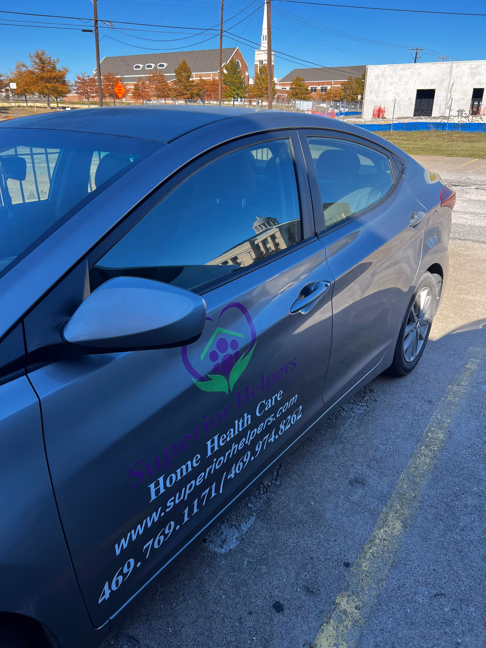 Gray car with Superior Helpers Home Health Care logo parked outdoors.