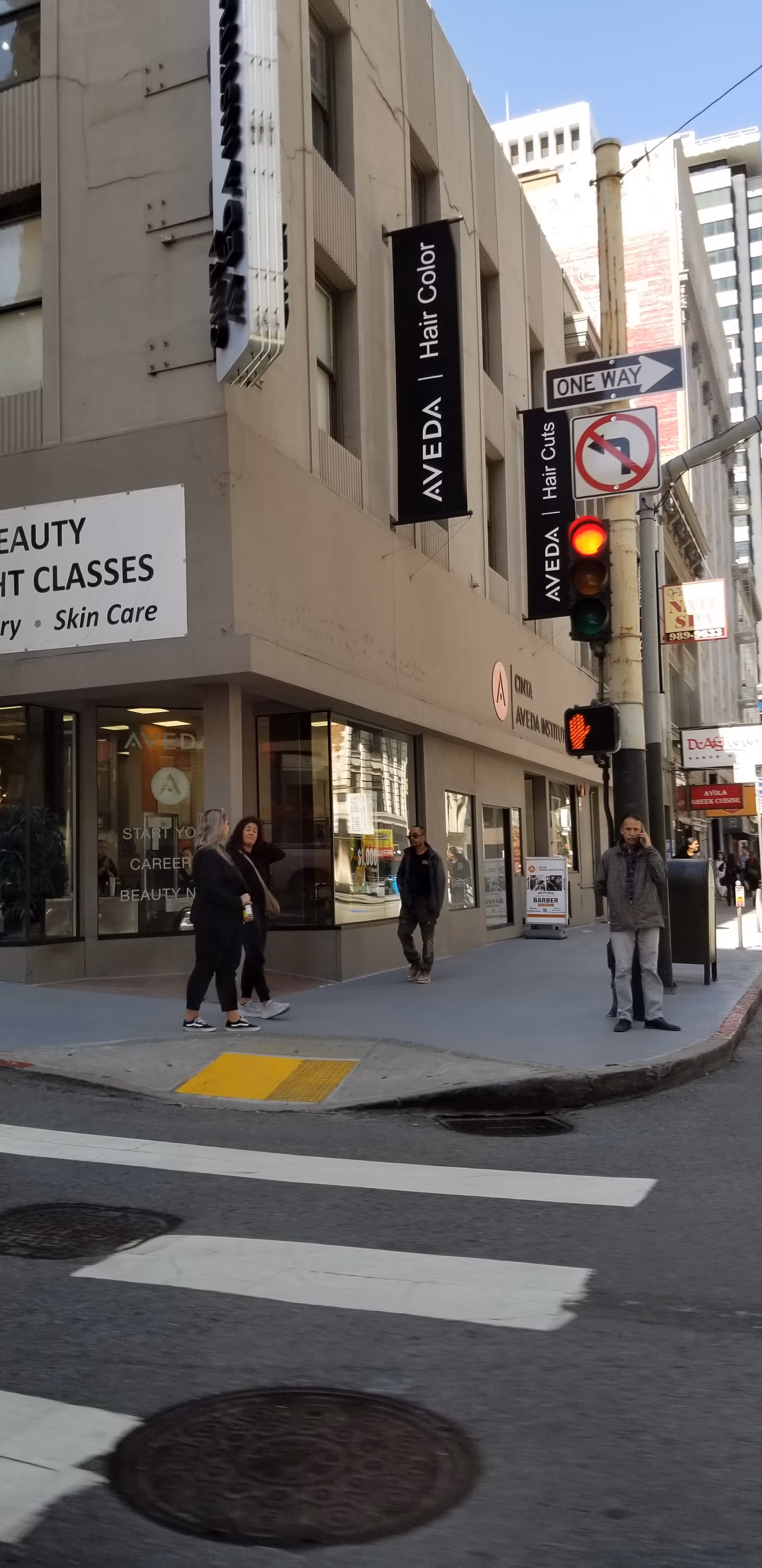 Urban street corner with storefronts, pedestrians, and traffic signals.