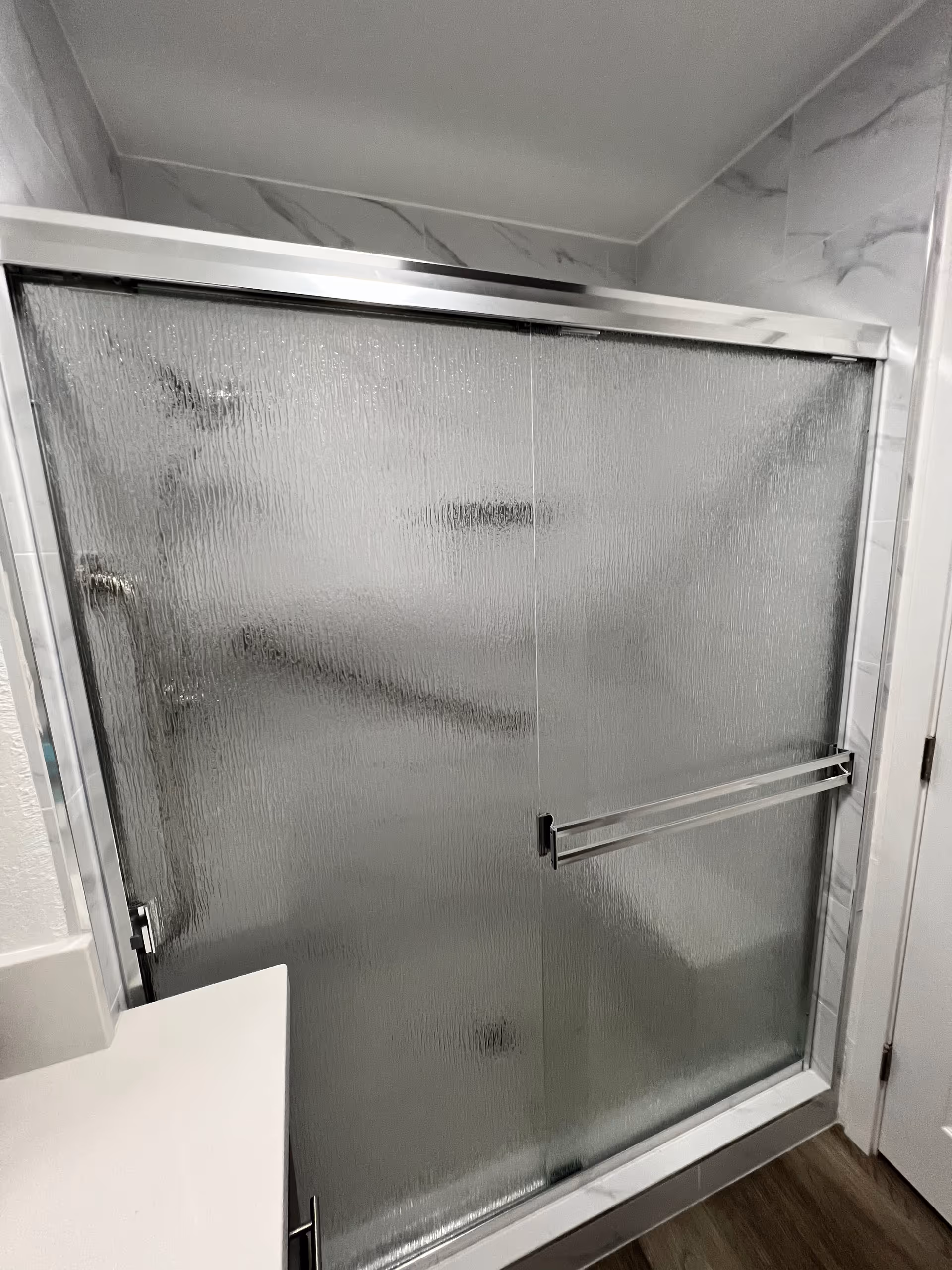 Shower with frosted glass doors in a marble-tiled bathroom.