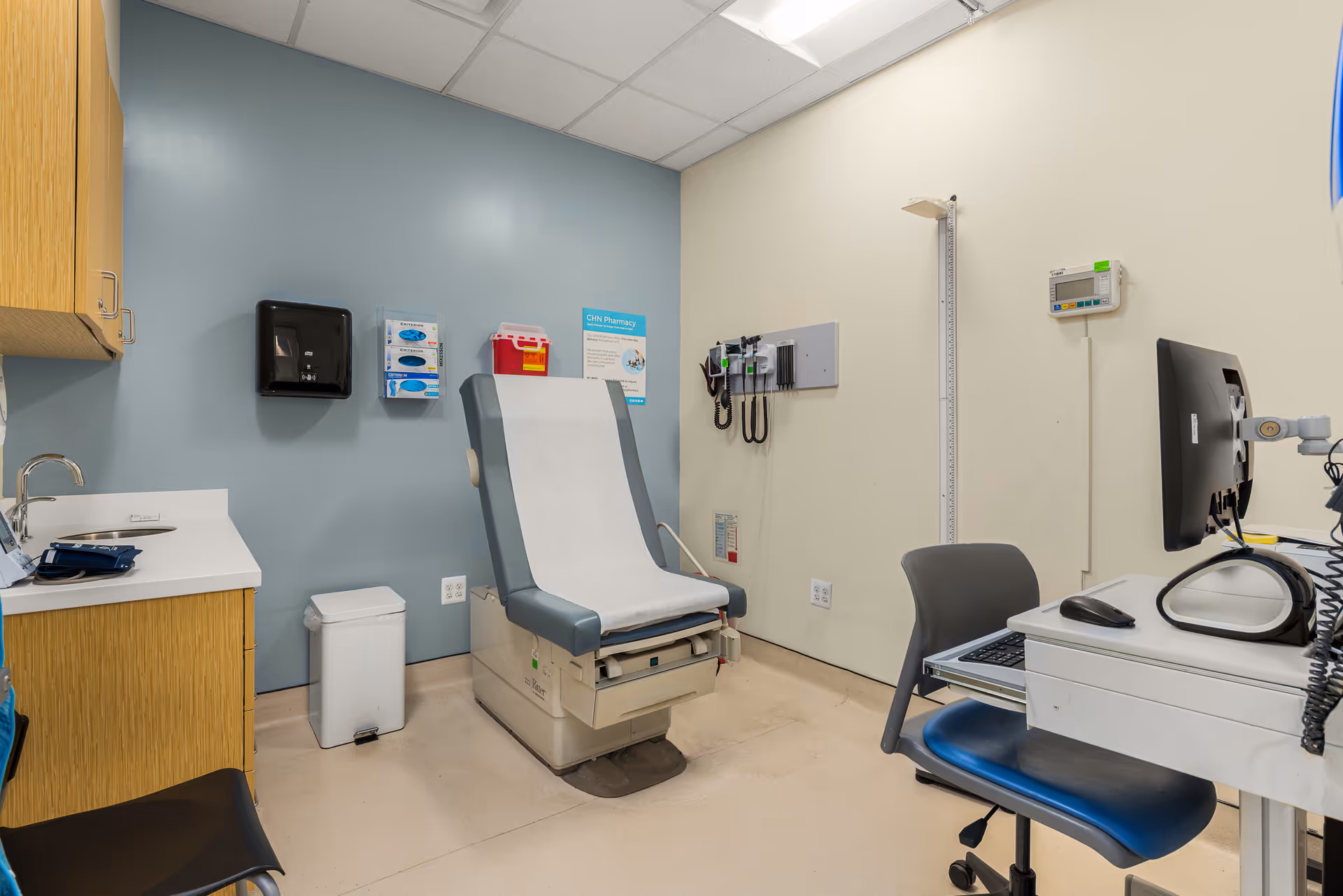 Medical examination room with chair, computer station, cabinets, and medical supplies.