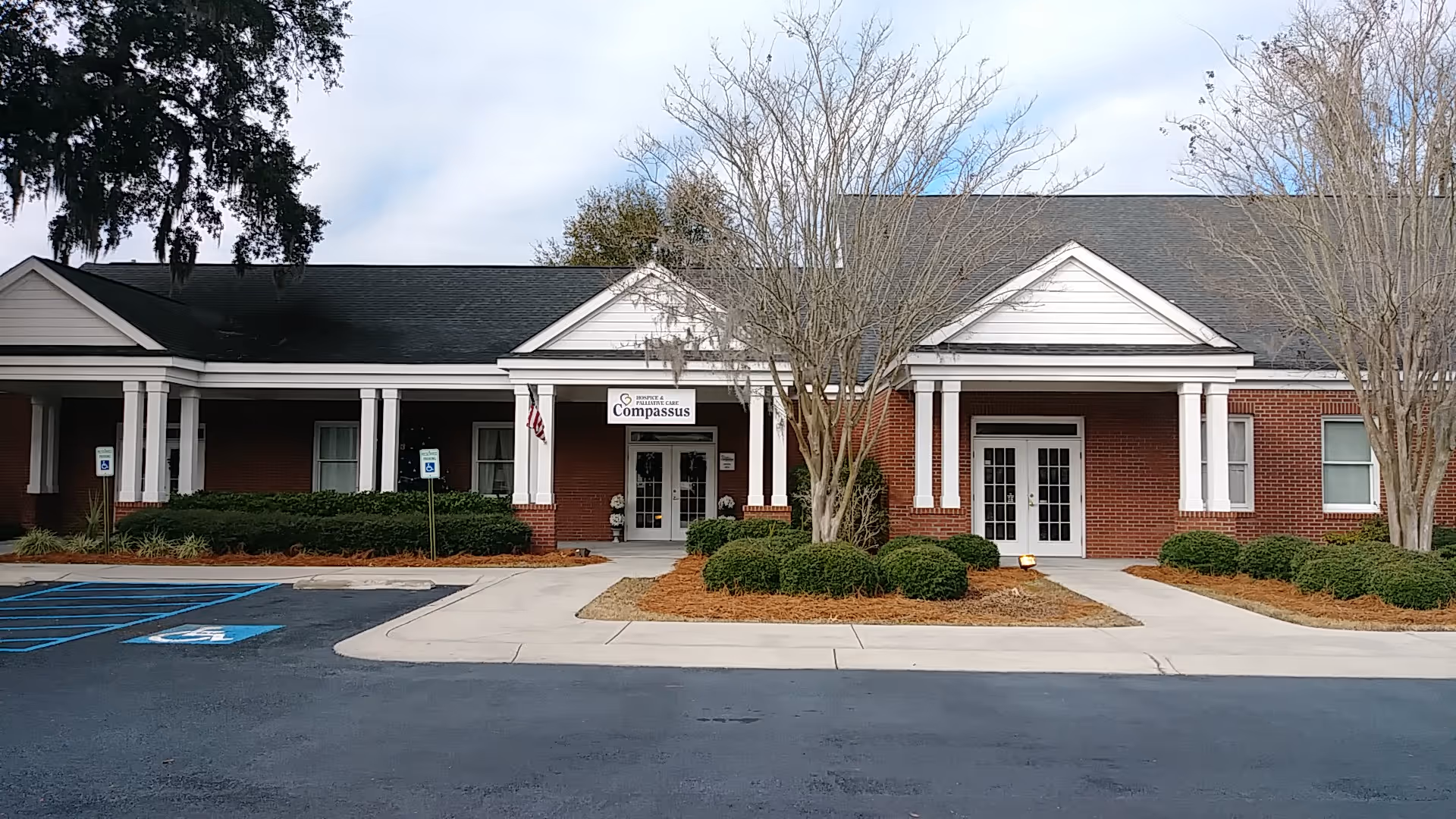 Exterior view of Compassus senior living facility with brick walls, white columns, and a parking lot.