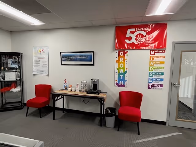 Reception area with two red chairs, a coffee station, and a BAYADA banner.