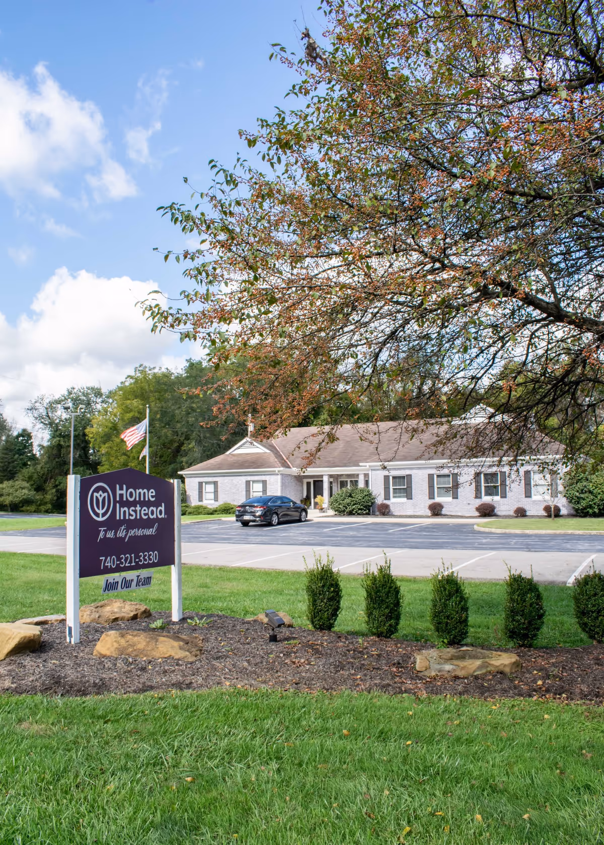 Exterior view of a Home Instead senior living facility with sign and parking.