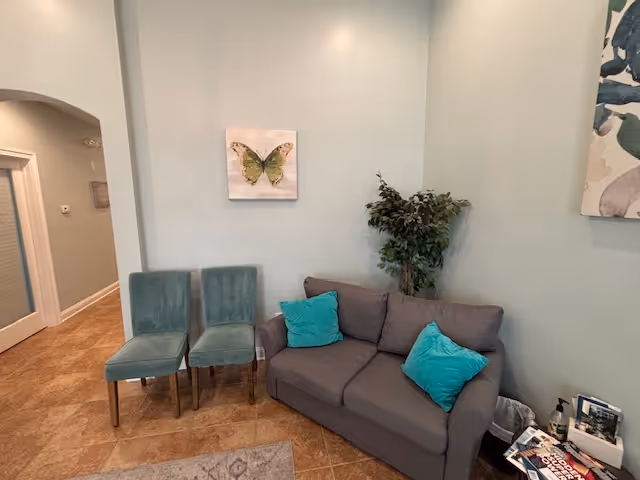 A cozy living room with gray sofa, teal chairs, turquoise pillows, and a plant.