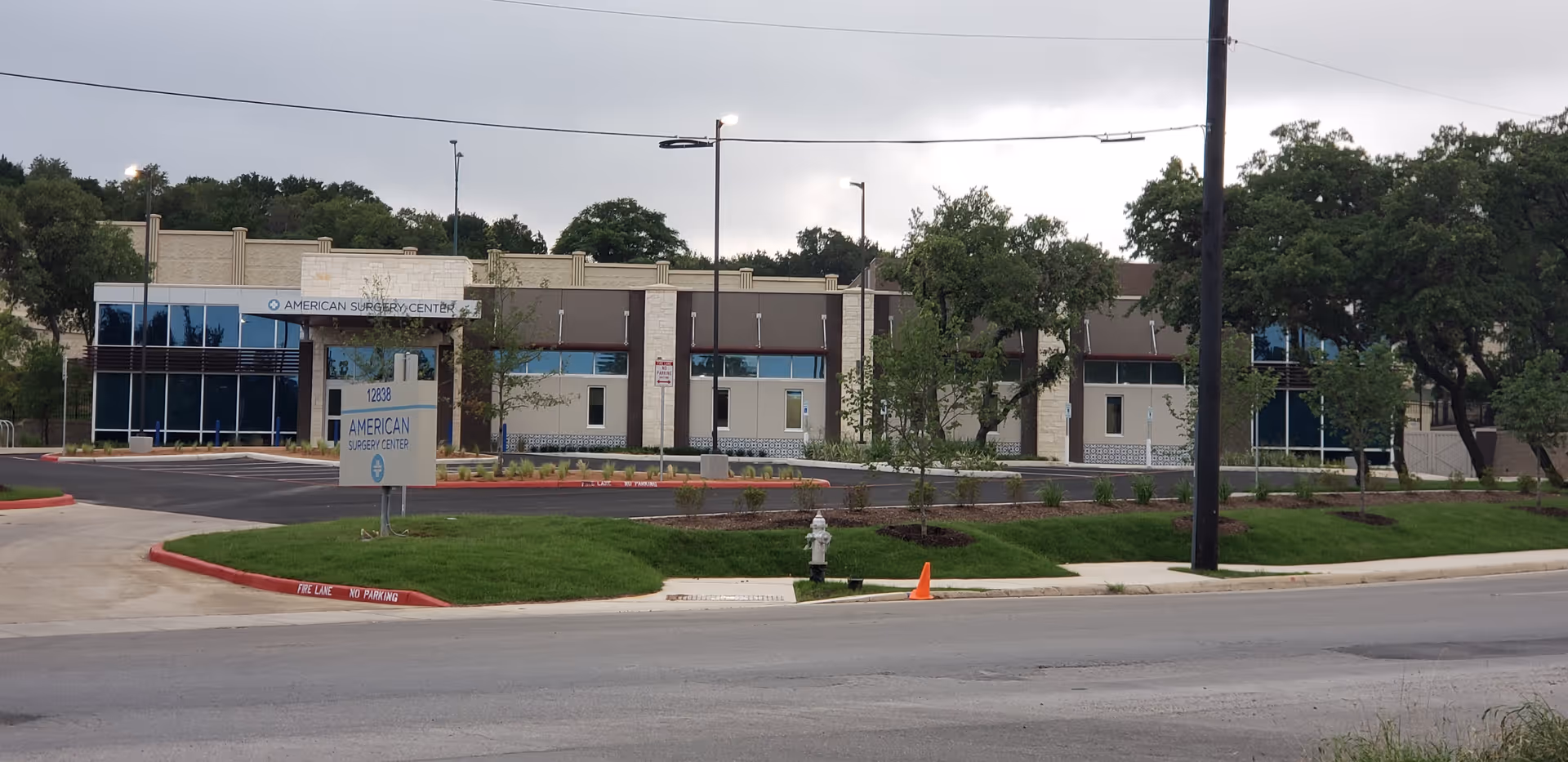 Exterior view of American Surgery Center of South Texas with parking lot and trees.