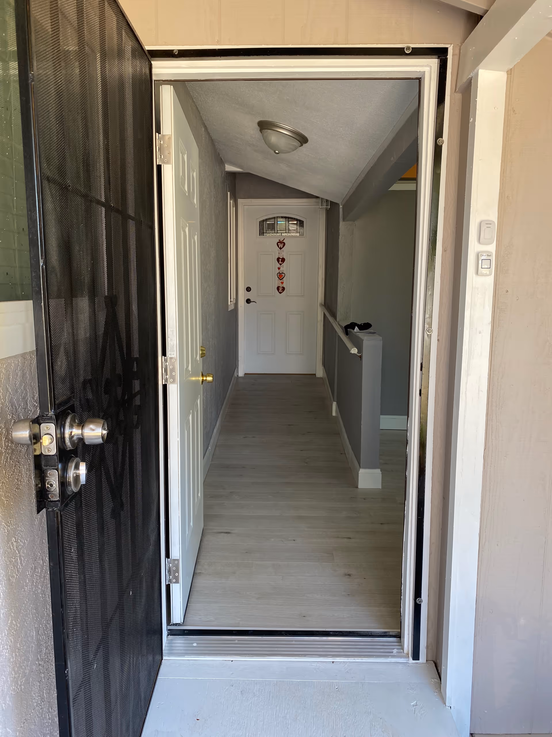 Open front screen door leads to a narrow interior hallway with white doors.