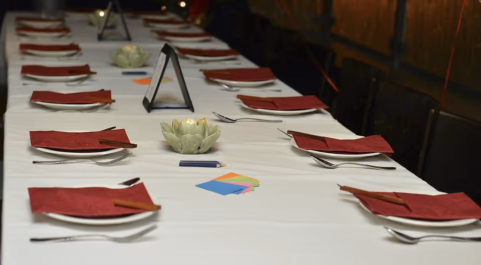 Long dining table set for guests with plates, utensils, red napkins, and centerpieces.