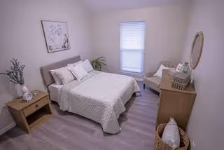 Tidy bedroom in a senior facility with a bed, dresser, window, and plants.
