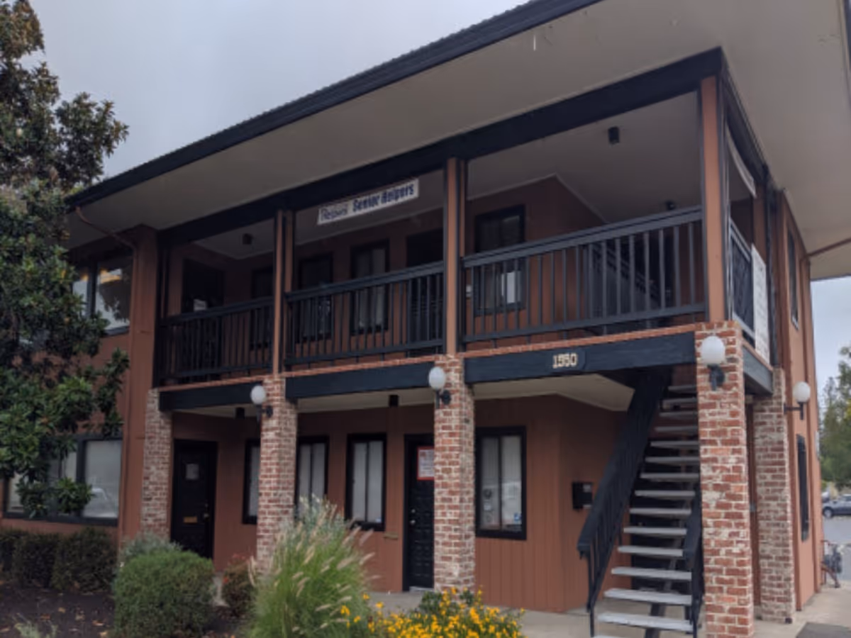 Two-story brick building with a balcony and stairs, labeled Senior Helpers, front entrance.