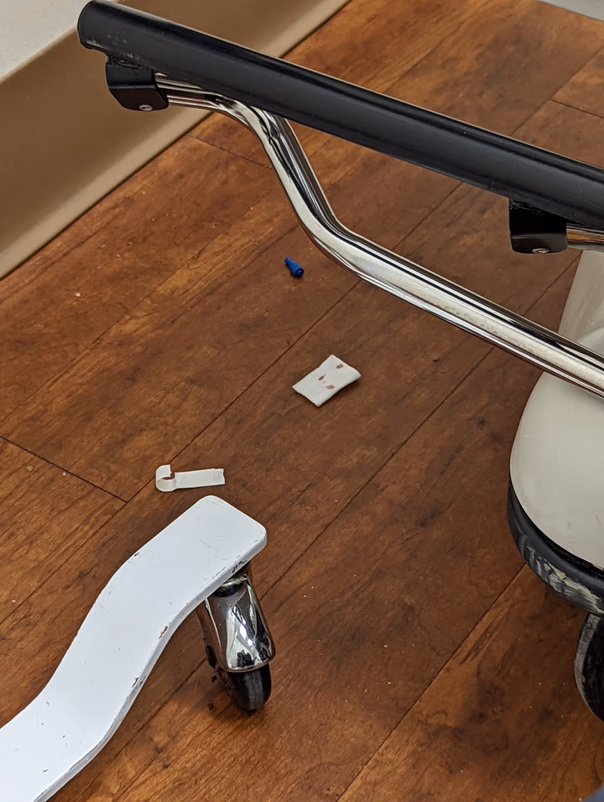 Close-up of a broken white mobility aid on a wooden floor inside.