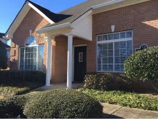 Front exterior of a brick senior living facility with a covered entry and shrubs.