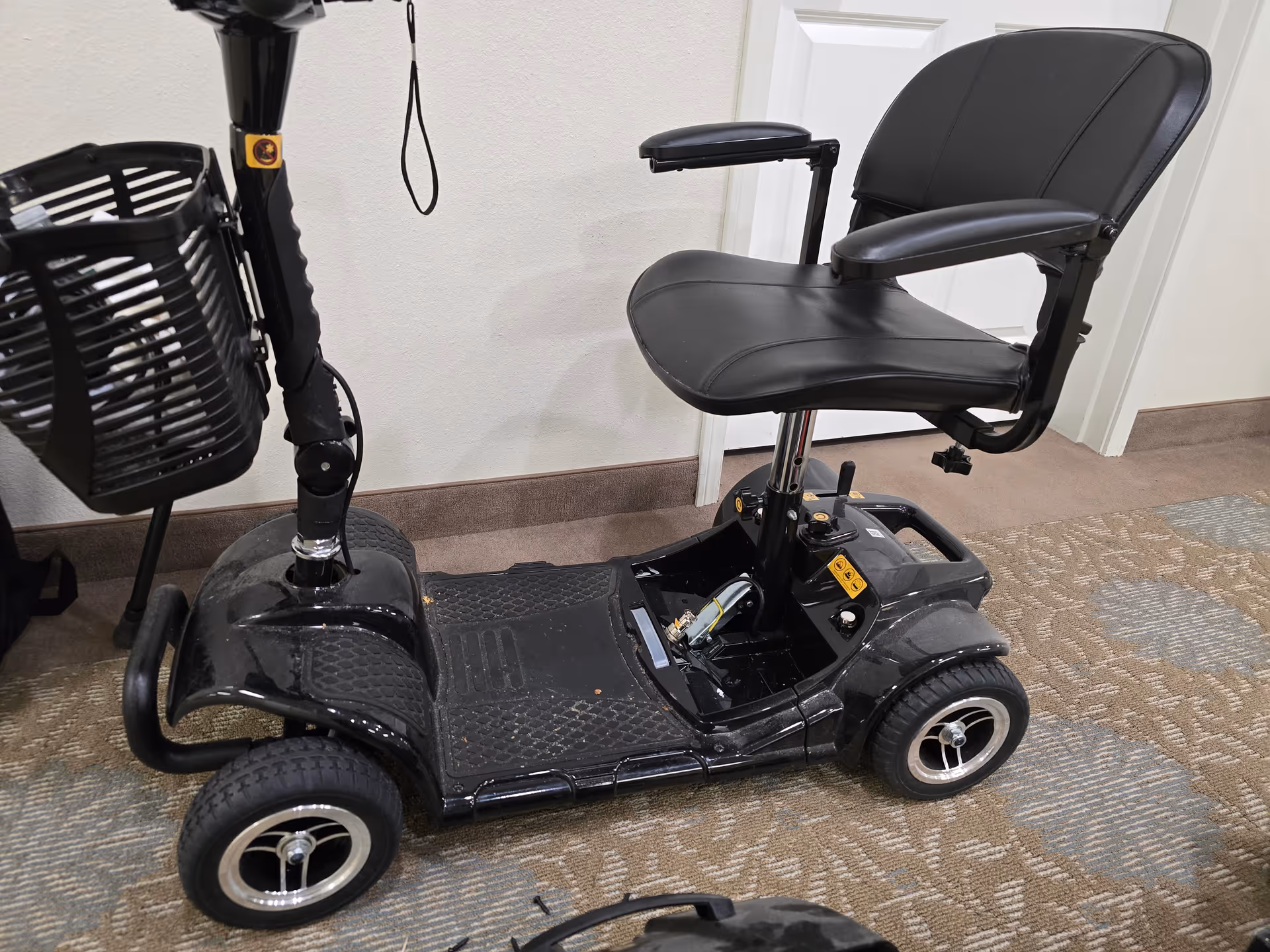A black mobility scooter sits indoors on a carpeted floor near a door