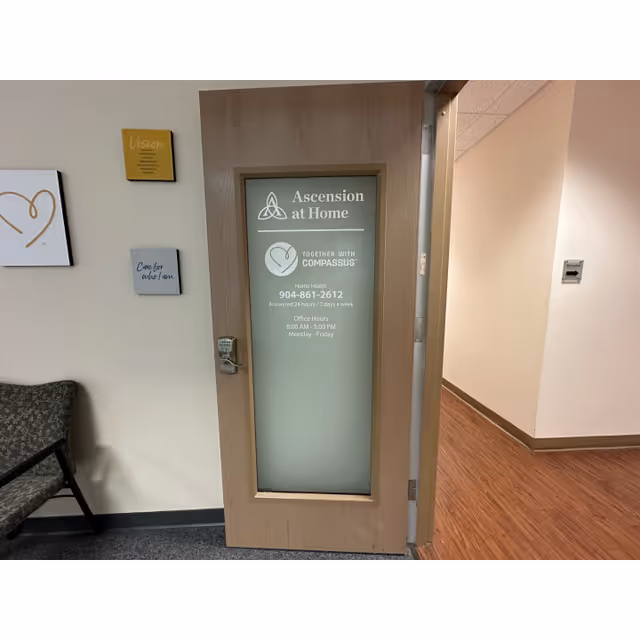 Wooden-framed door with frosted glass sign reads 'Ascension at Home' in a hallway.