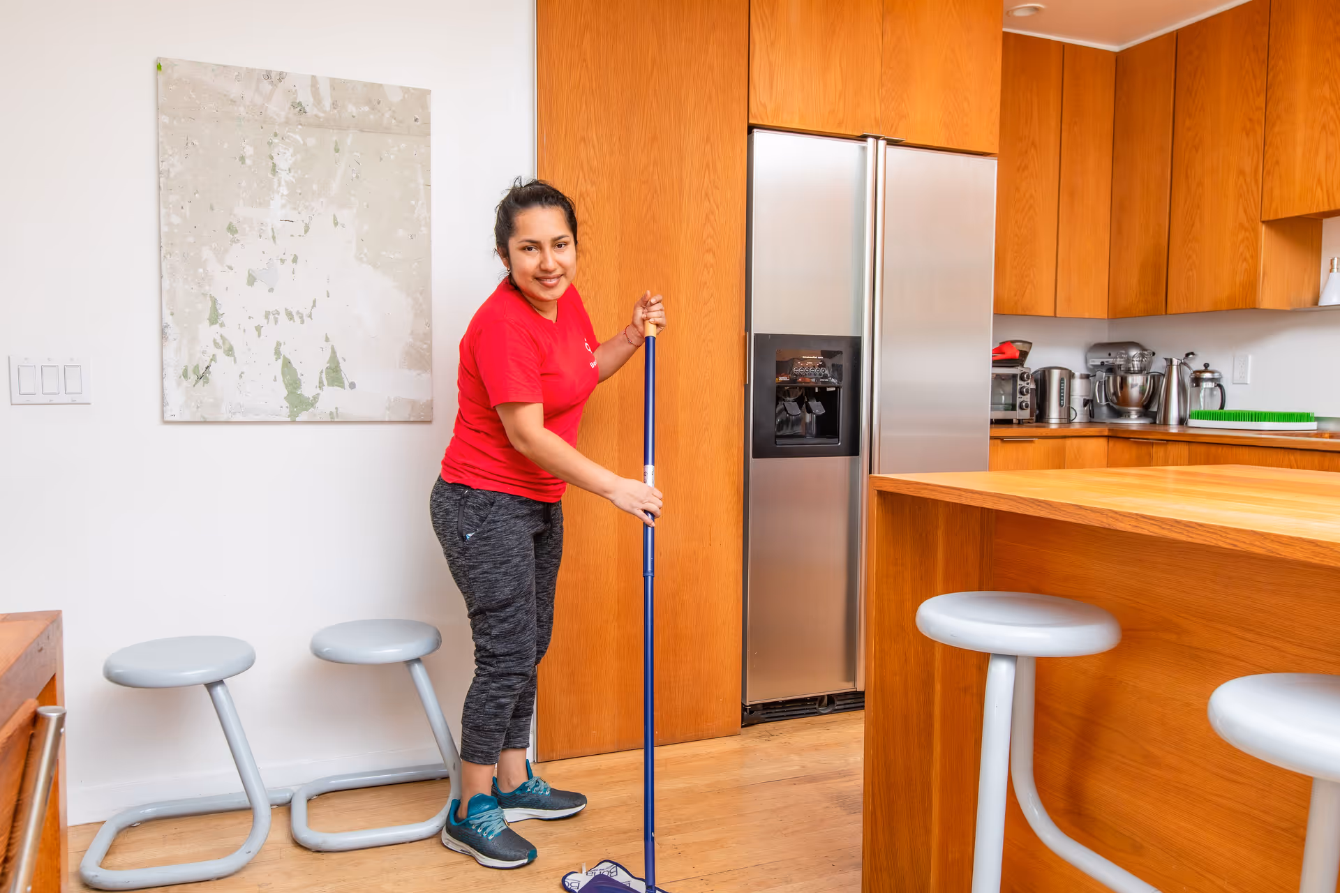 Staff member in red shirt mopping a modern kitchen with wooden cabinets and island