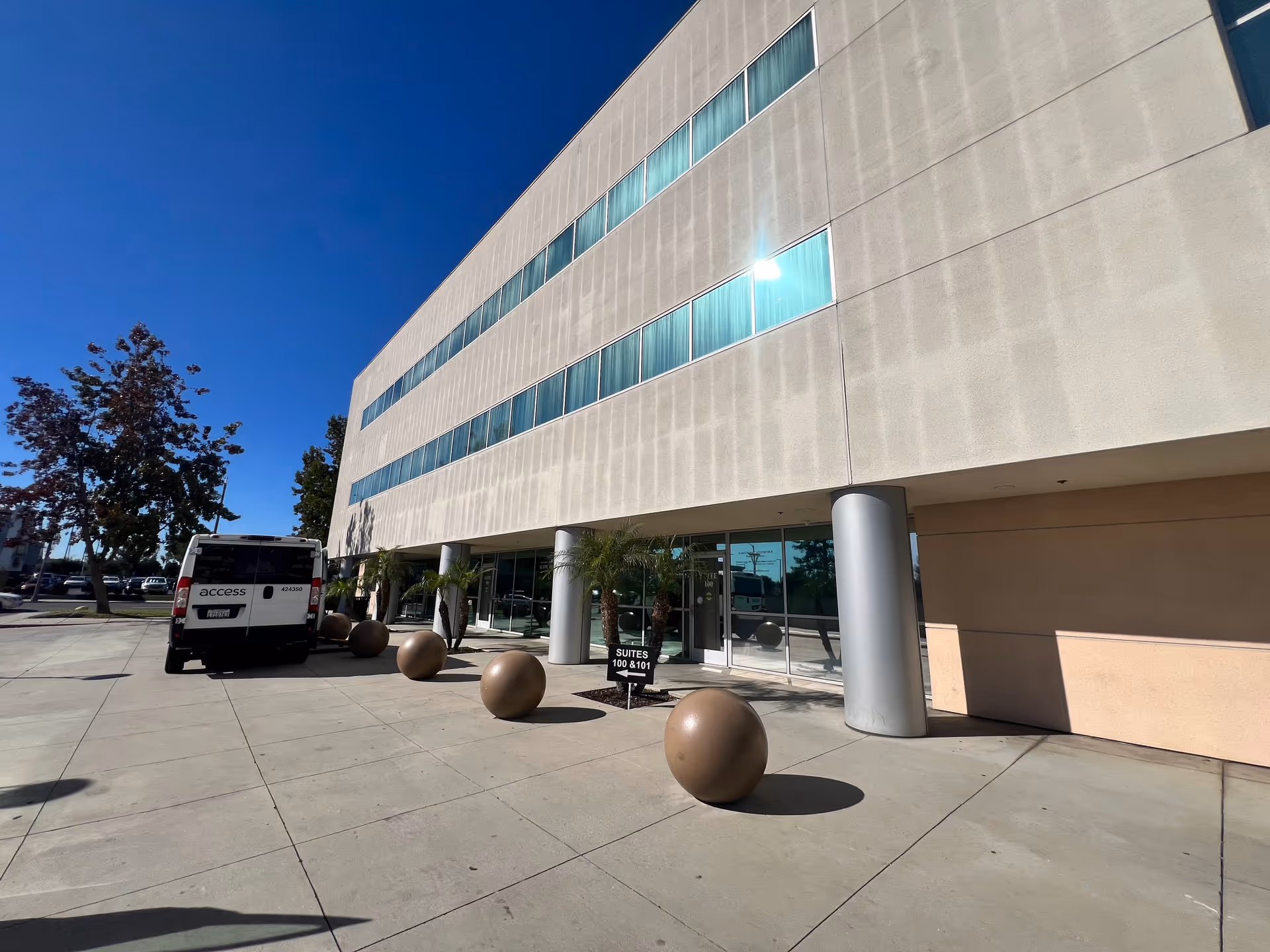 Modern beige commercial building front with glass entrance and a parked van