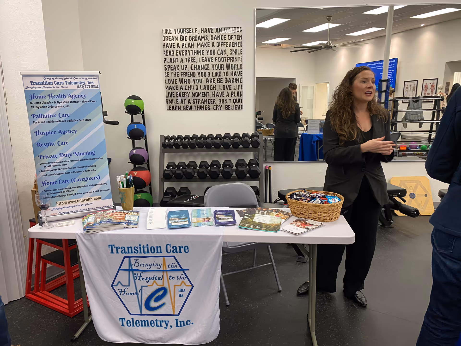 A woman talks beside a Transition Care Telemetry table in a gym-like interior.