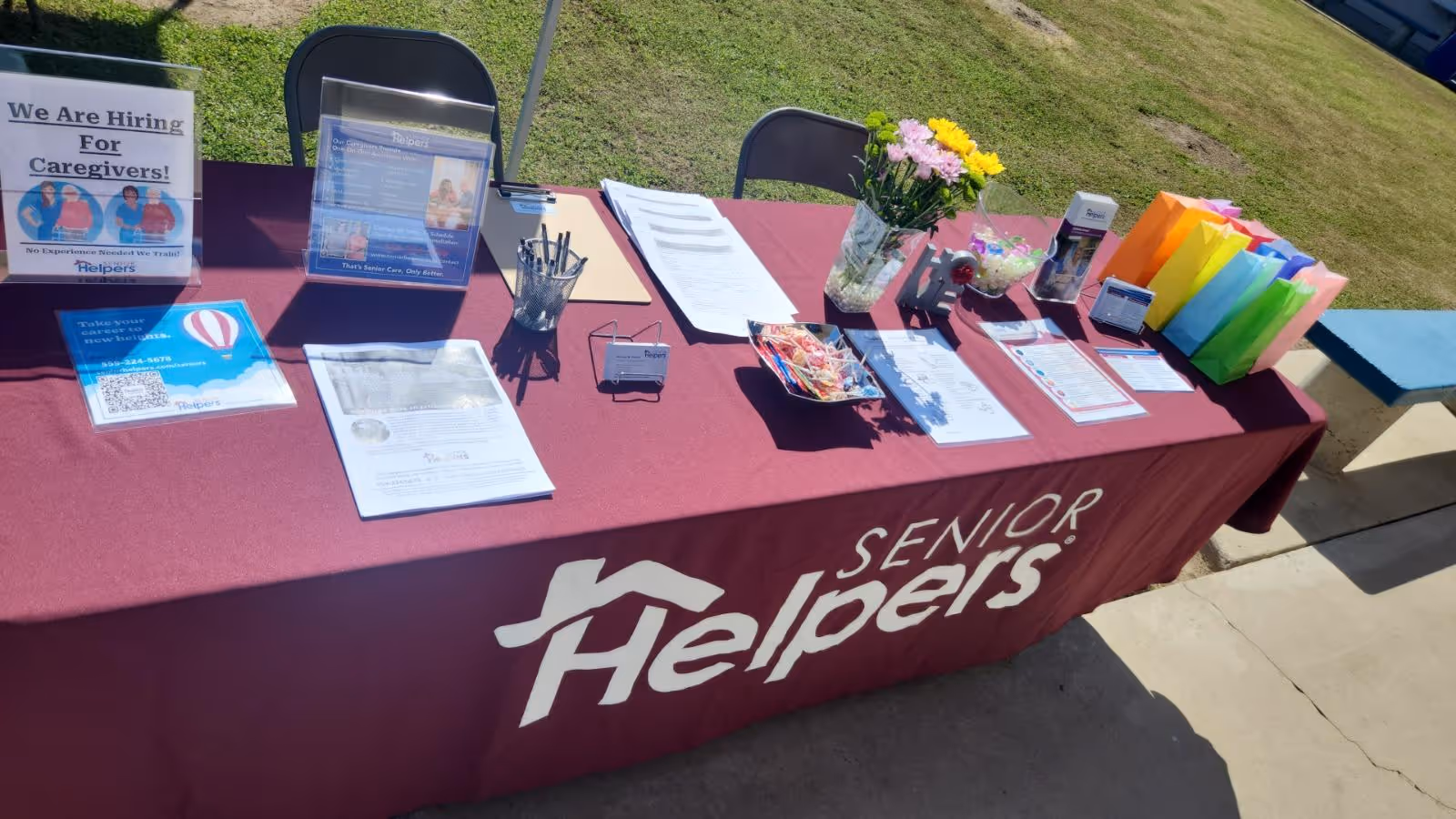Outdoor Senior Helpers promotional table with brochures, flowers, and colorful gift bags.