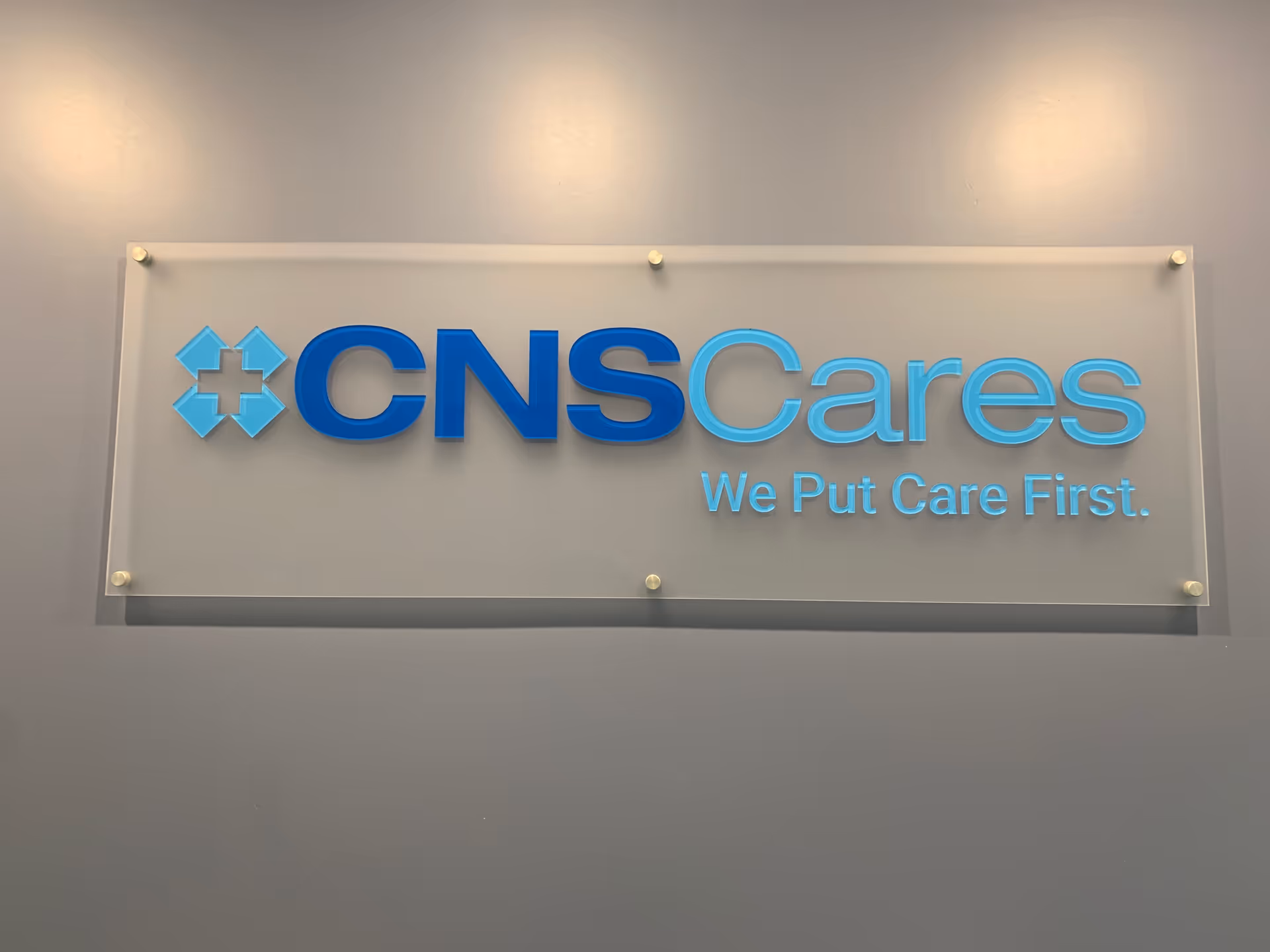 Blue CNS Cares sign on a gray interior wall with slogan We Put Care First