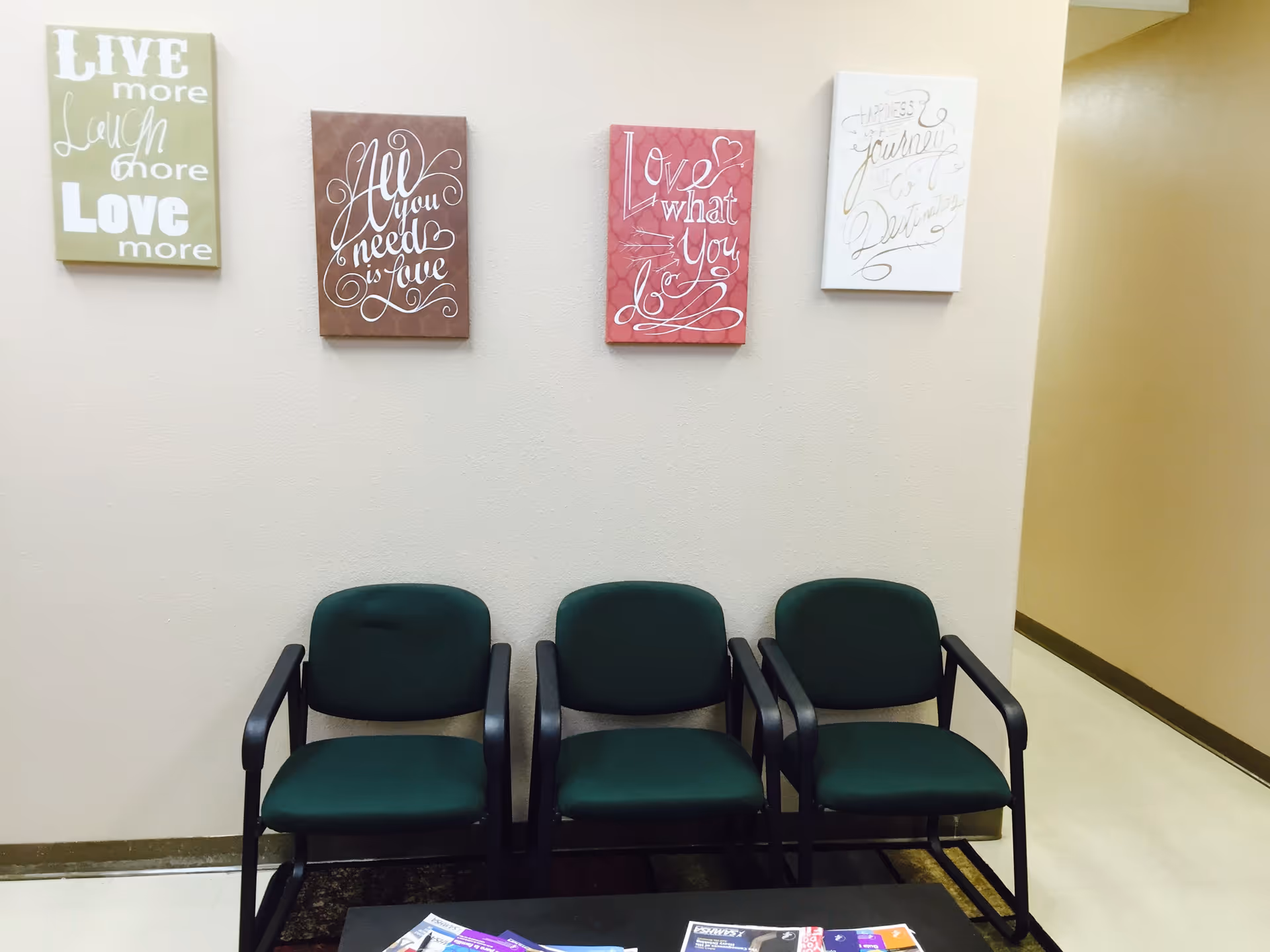 Four green chairs line a wall with decorative quotes above in a waiting area.