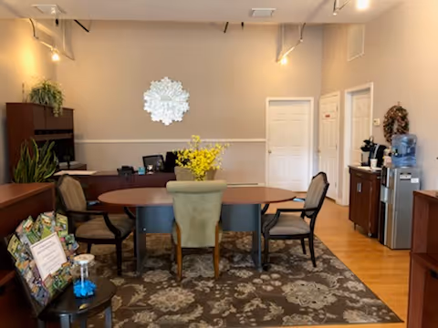 Cozy interior common area featuring a round table, chairs, plants, and a water cooler.