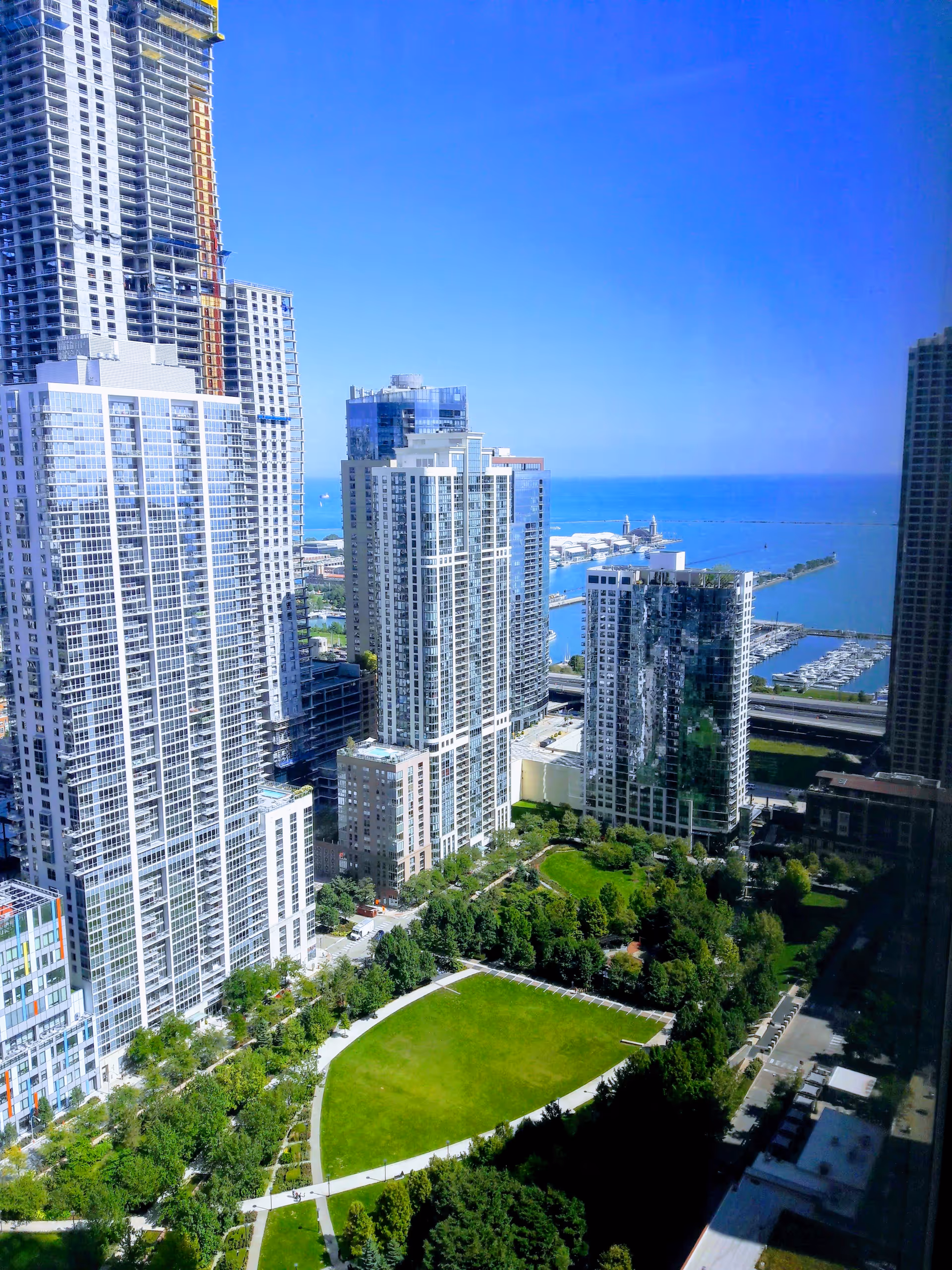 View of tall glass skyscrapers surrounding a green park by the waterfront.