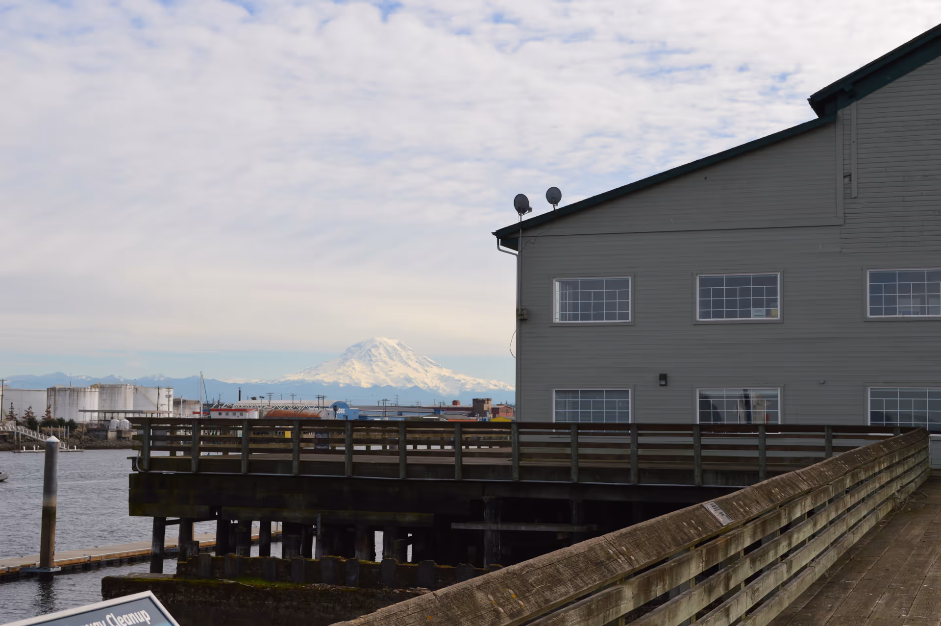 Gray multi-story building beside a wooden pier over water with distant mountains.