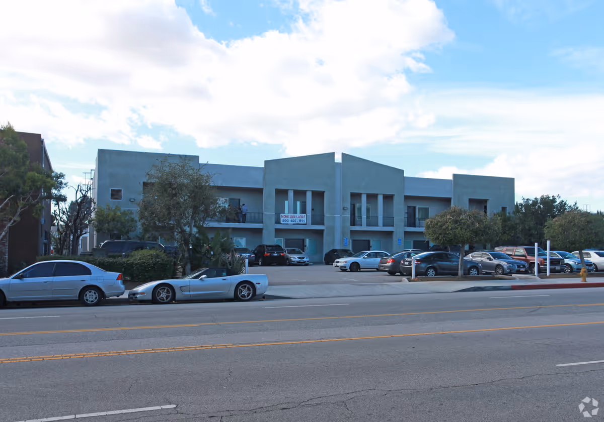 Blue modern building with parked cars and a clear sky.