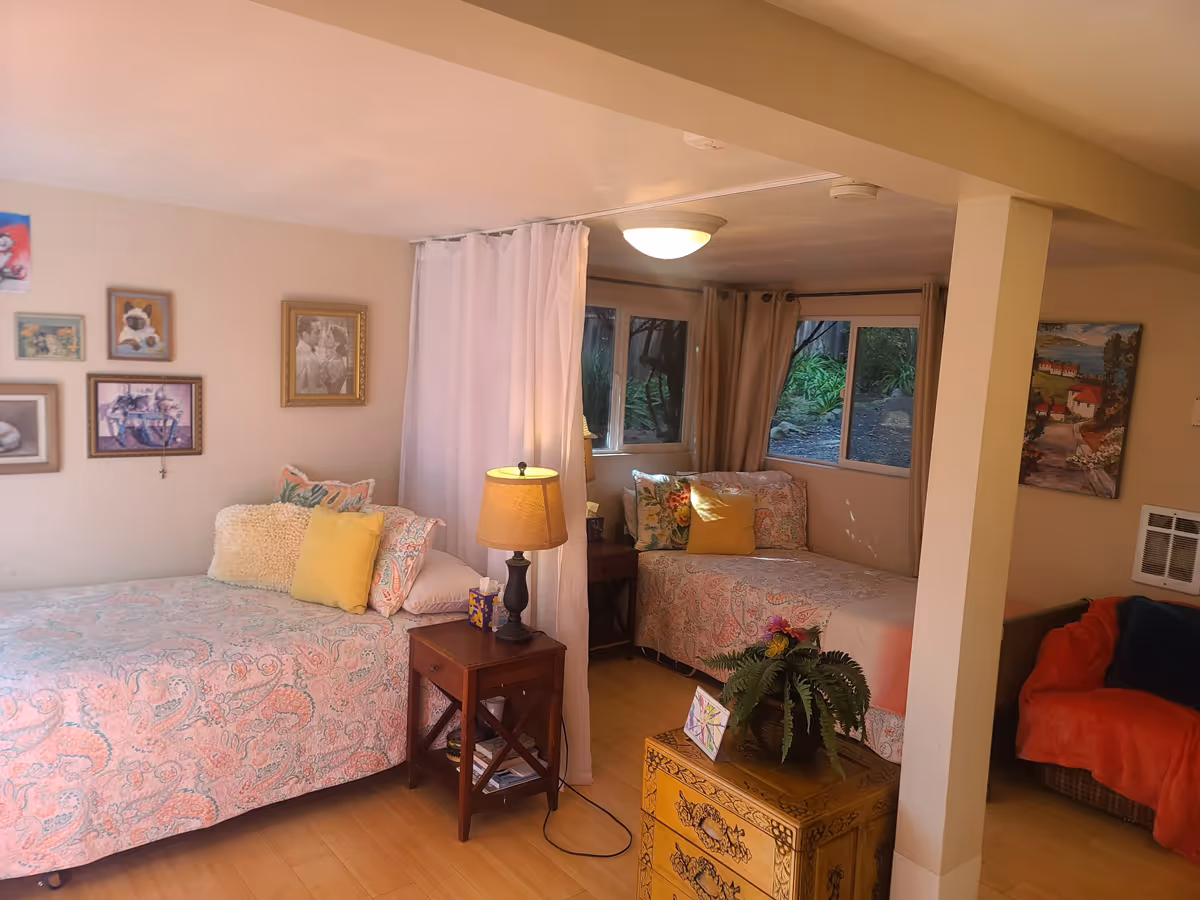 Two beds separated by a white curtain in a cozy beige bedroom area.