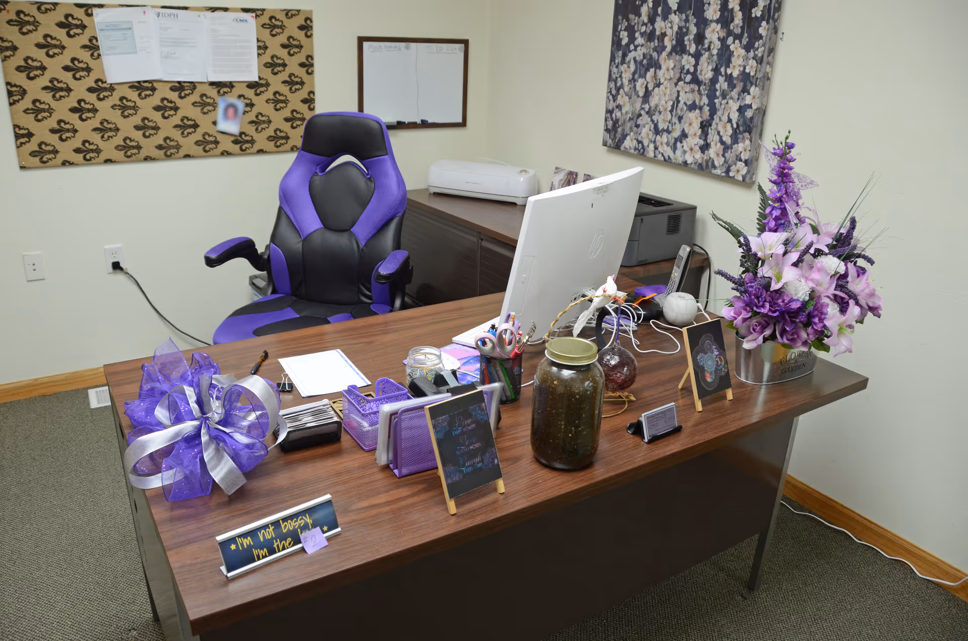 Office desk with purple accents, flowers, and computer in a hospice administrative space.