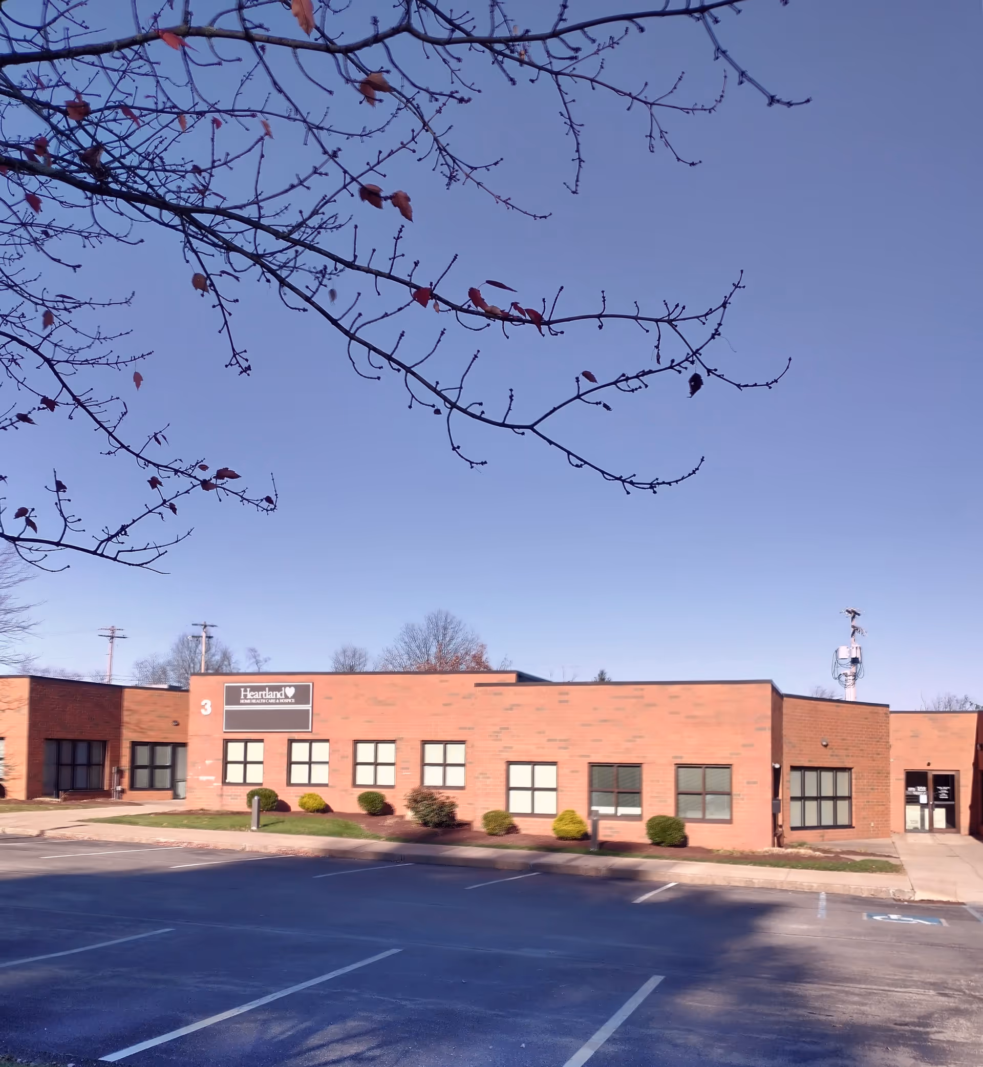 Exterior view of a brick Heartland Hospice building with parking lot and clear sky.