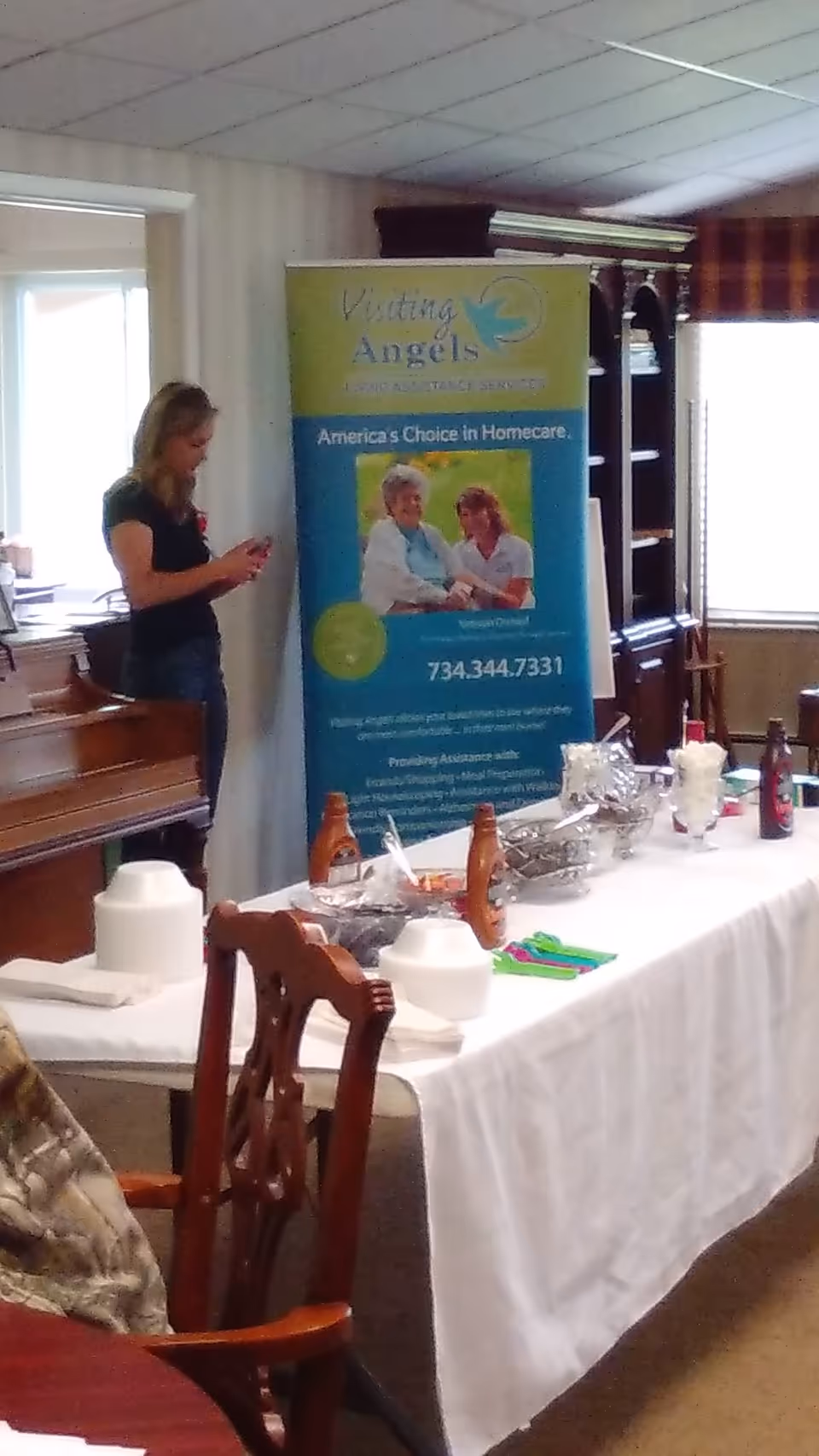 Indoor event area with a Visiting Angels banner, table setup, and a standing woman.