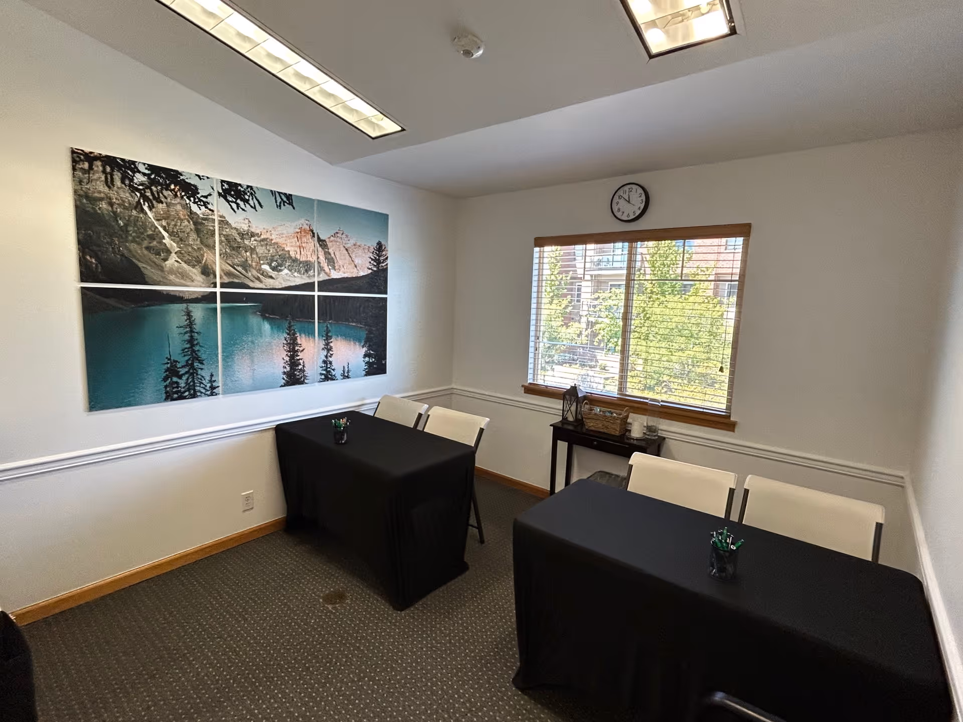 Two black-clothed tables with white chairs in a small conference room beside a window.