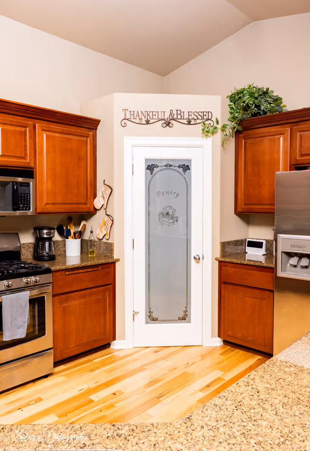 Warm kitchen with wooden cabinets, stainless appliances, and a frosted pantry door.
