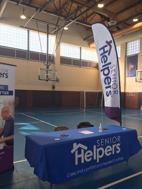 Indoor gym setup with a Senior Helpers table, banner, and a person nearby.