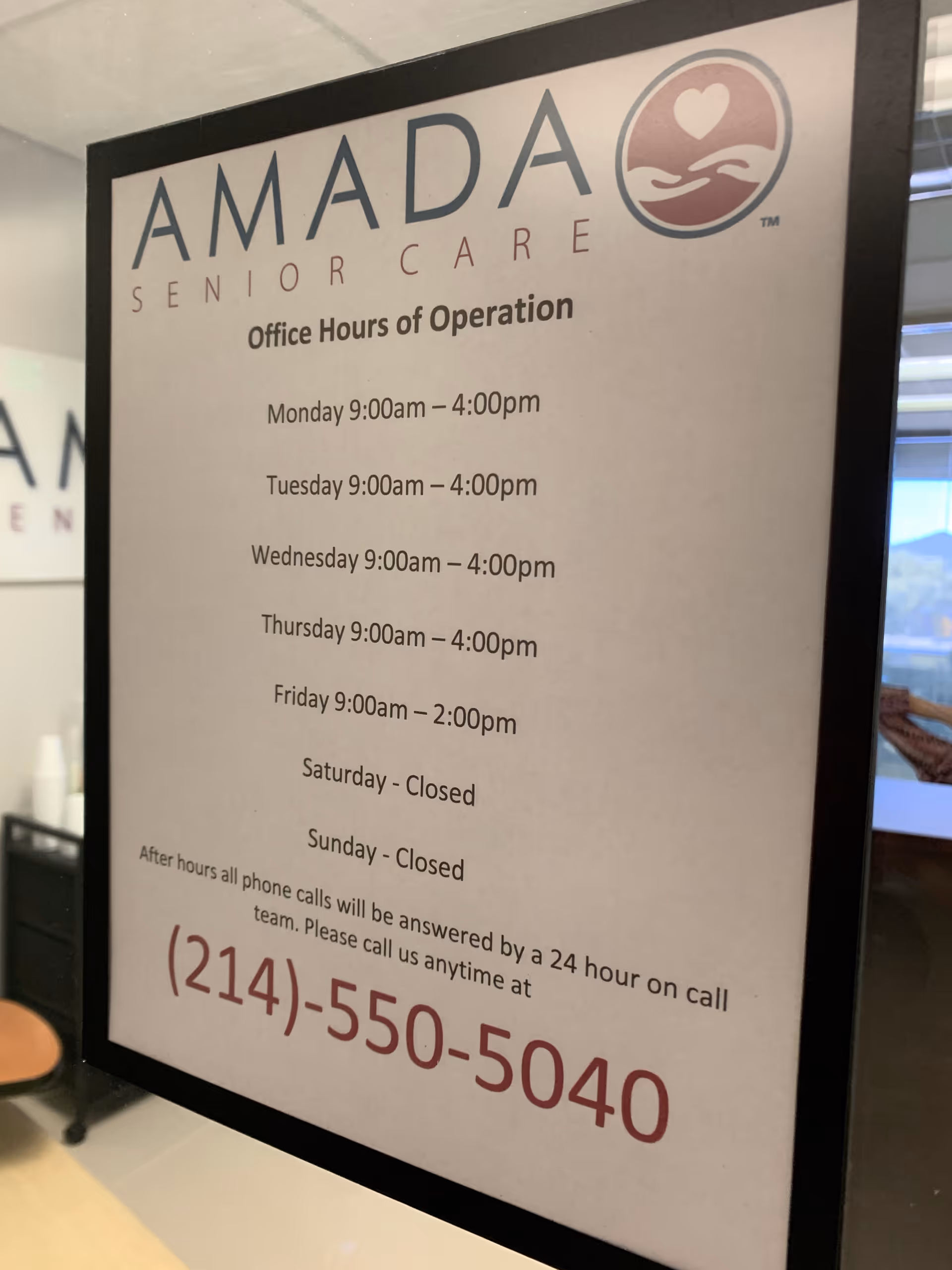 Framed Amada Senior Care office hours sign displayed inside a facility lobby.