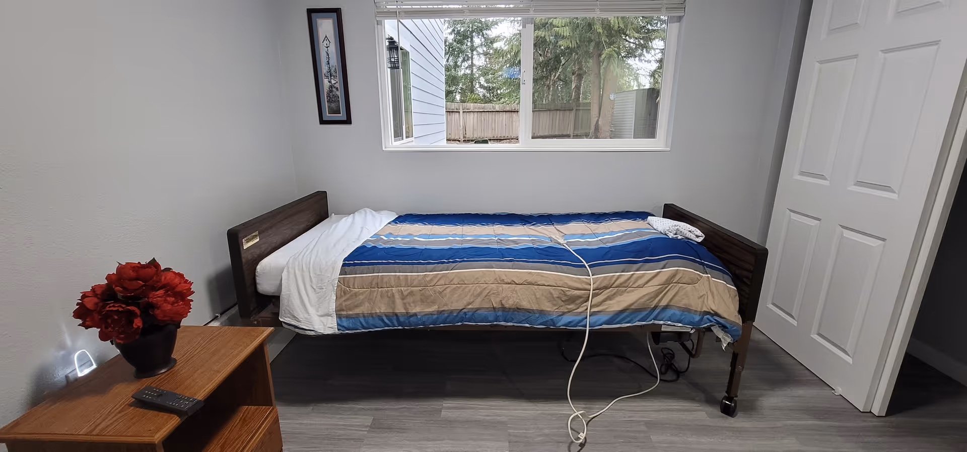 Small bedroom with a single bed, striped bedding, window, and nightstand with red flowers.