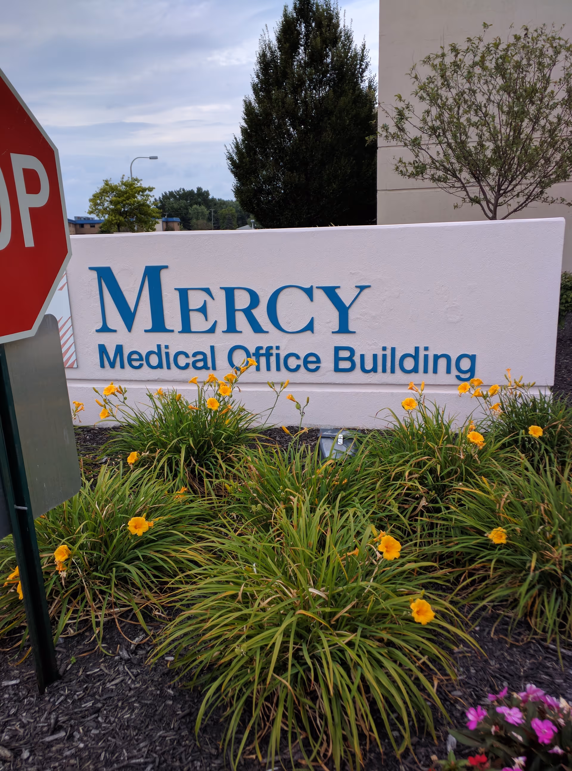 Mercy Medical Office Building sign with landscaping and flowers; stop sign visible.