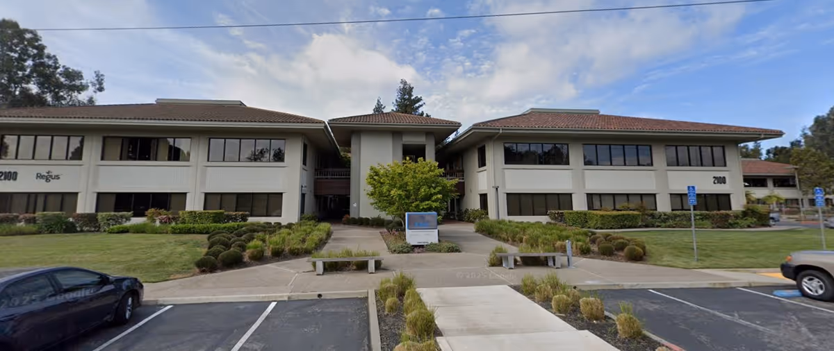 Two-story senior living building with manicured lawns, shrubs, and a central walkway.