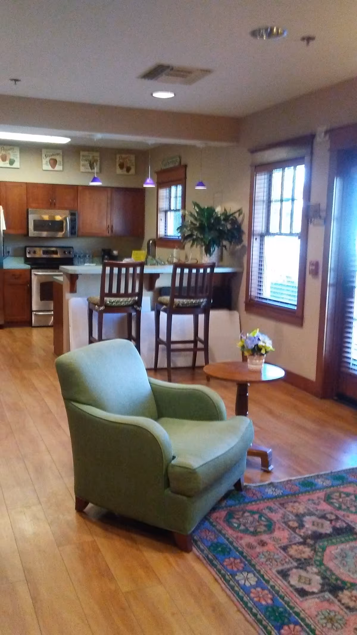 Open living area with a green armchair, small round table, and kitchen island with stools.