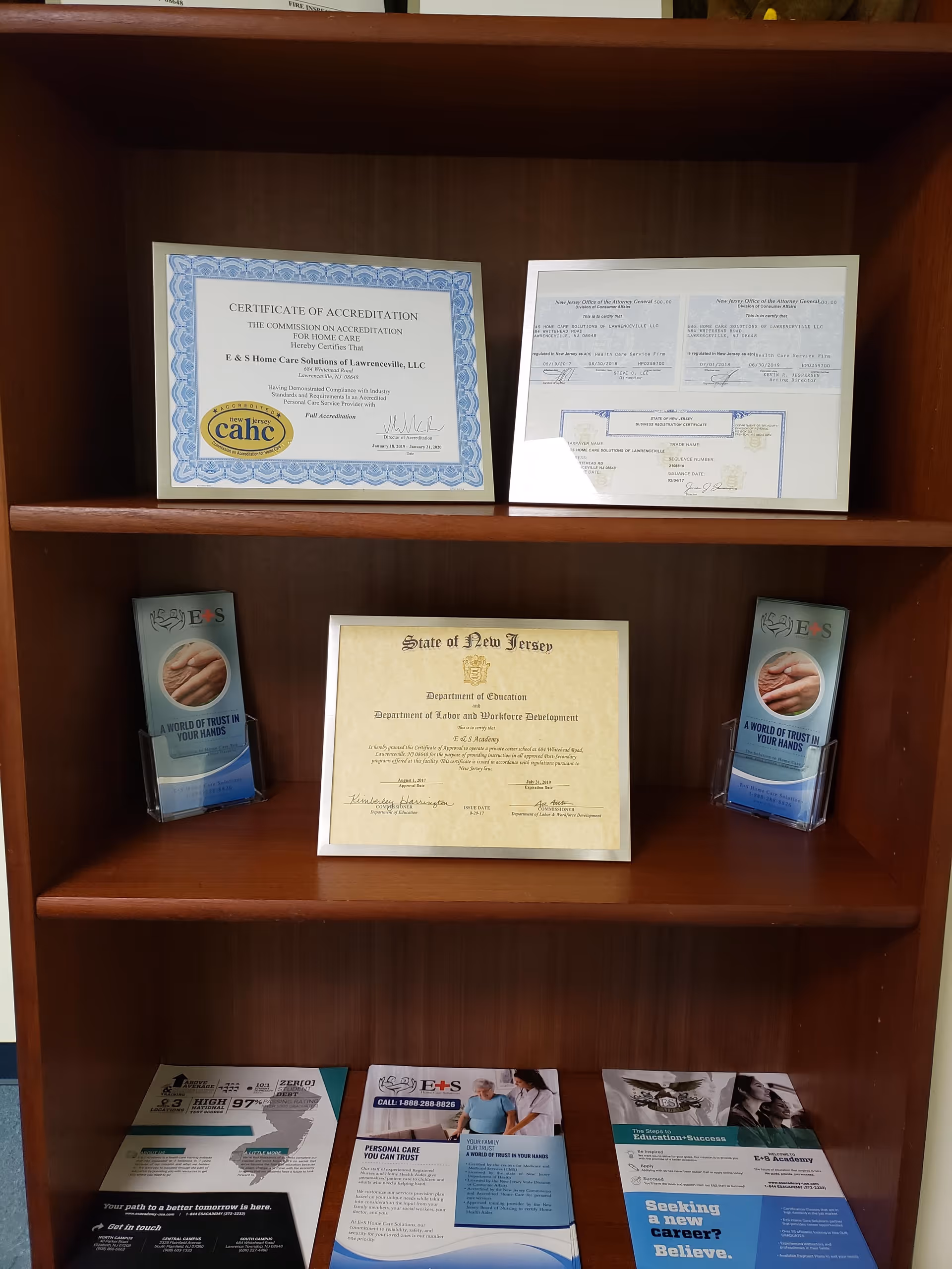 Wooden bookshelf with certificates and E&S Home Care Solutions brochures.