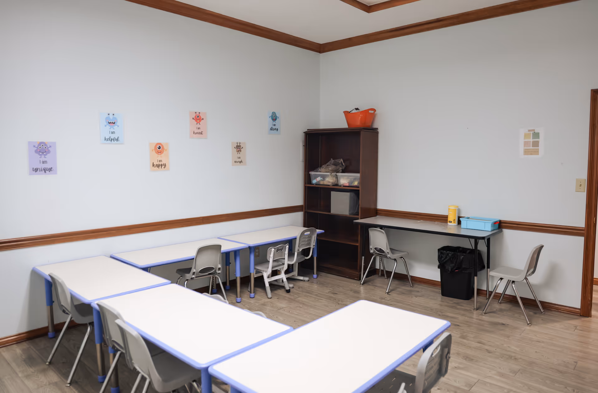 A classroom-style therapy room with small desks, chairs, and a storage cabinet.