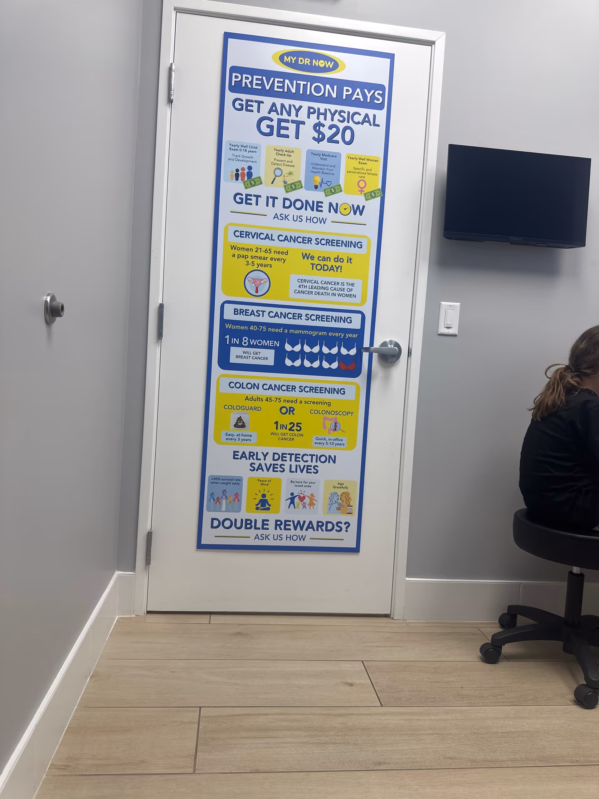Door with a large colorful health screening poster in a facility hallway, chair and monitor nearby.