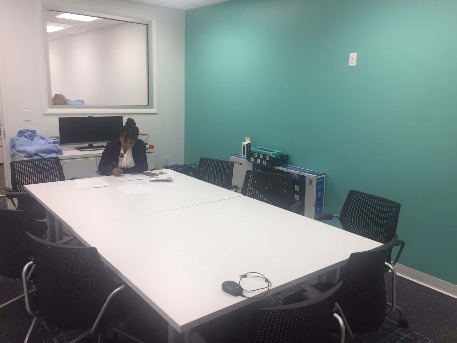 A staff member sits at a long white table signing papers in a bright meeting room.
