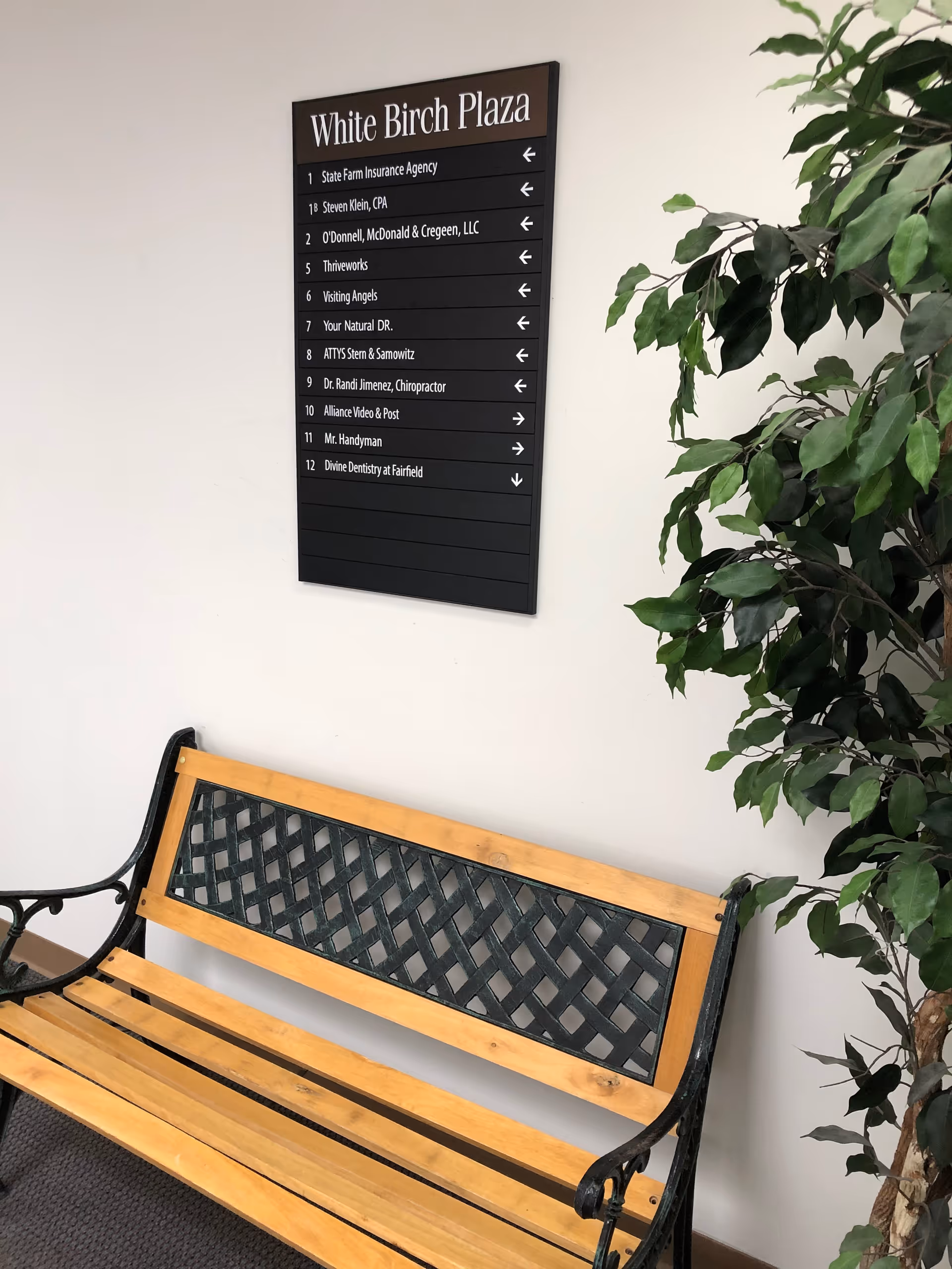 Indoor hallway with wooden bench, black directory sign, and leafy plant.