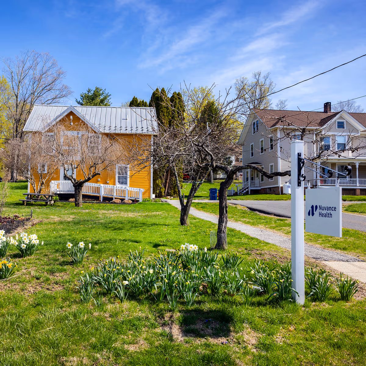 Exterior view of a yellow clinic with Nuvance Health sign and blooming flowers.