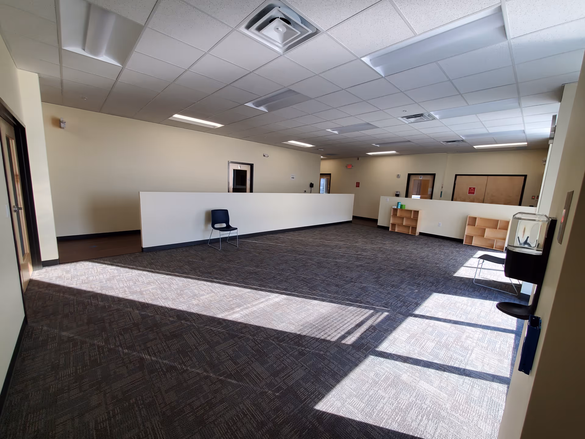 Bright interior lobby with a long white reception counter, shelving, and sunlit carpet.