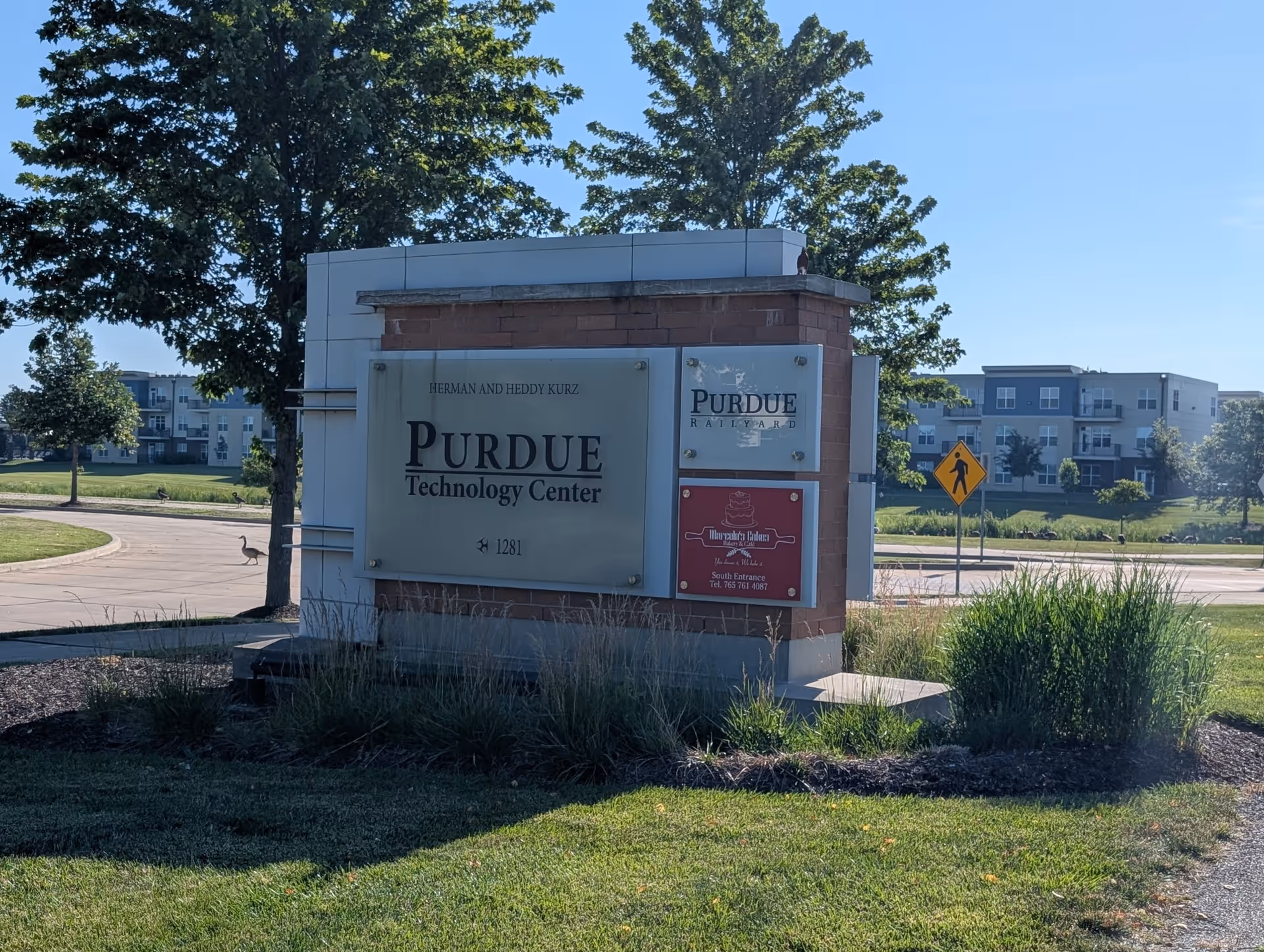 Outdoor sign structure for Purdue Technology Center with landscaping and nearby buildings.