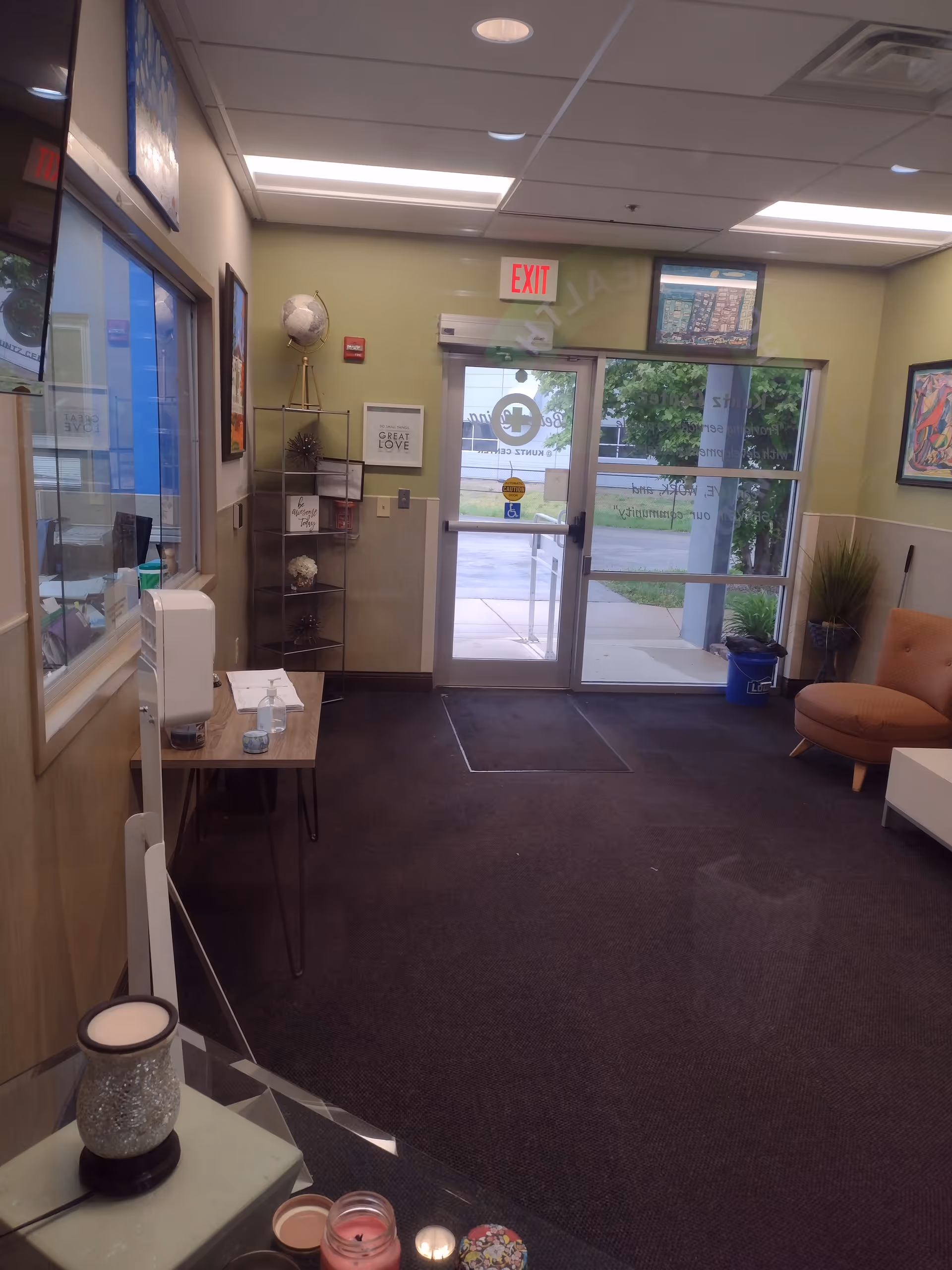 Interior facility lobby with seating, a small desk, decor shelves, and glass exit doors.