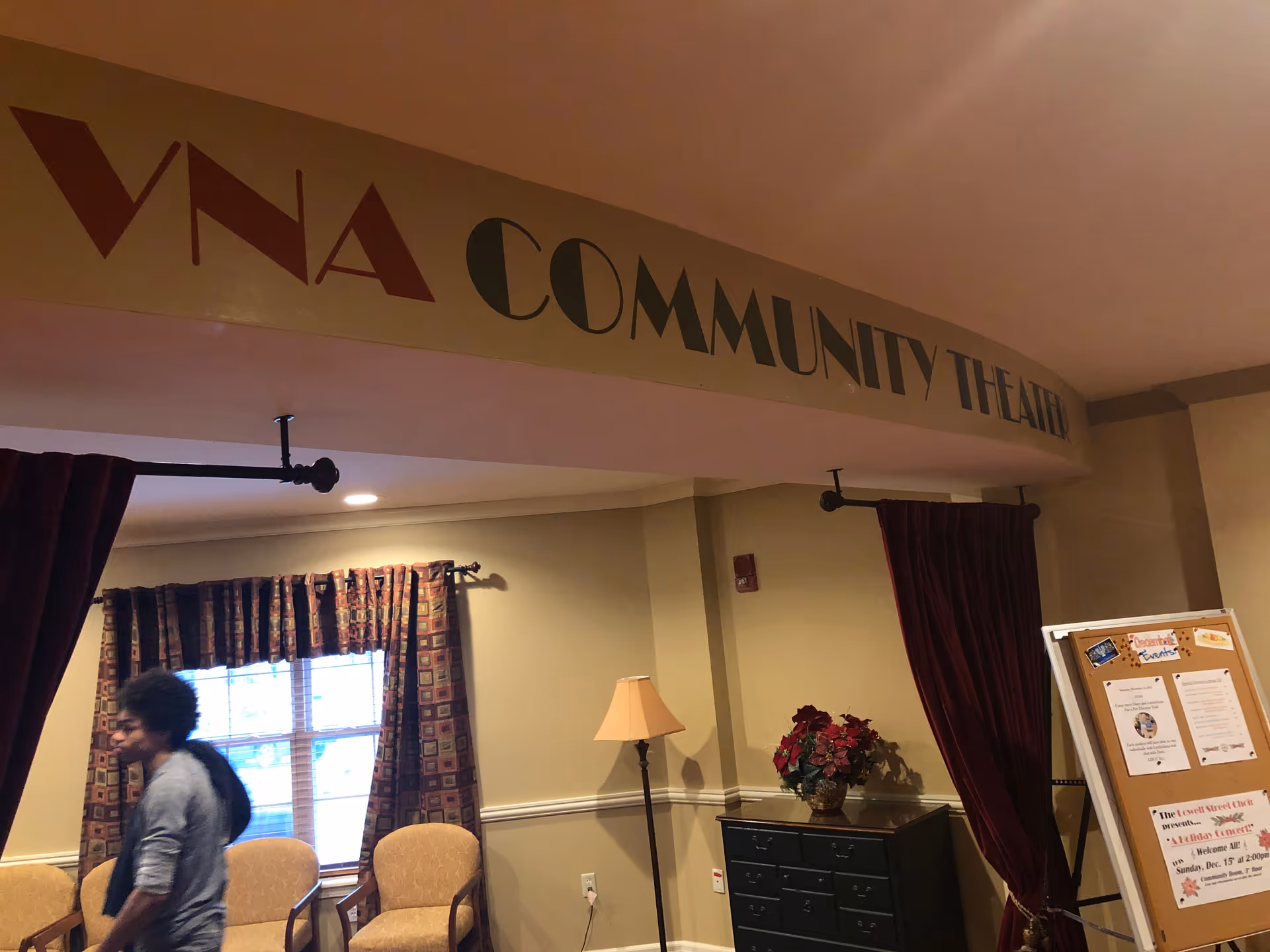 Interior of VNA Community Theater with chairs, curtains, bulletin board, and a person.